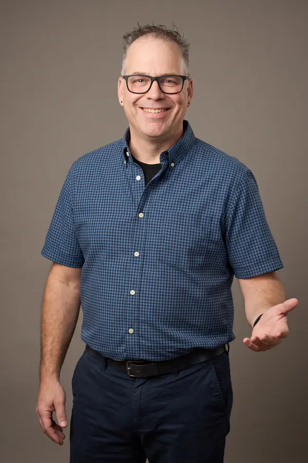 Portrait de François Paradis, de FP Service, souriant, en chemise à carreaux bleue, la main ouverte.
